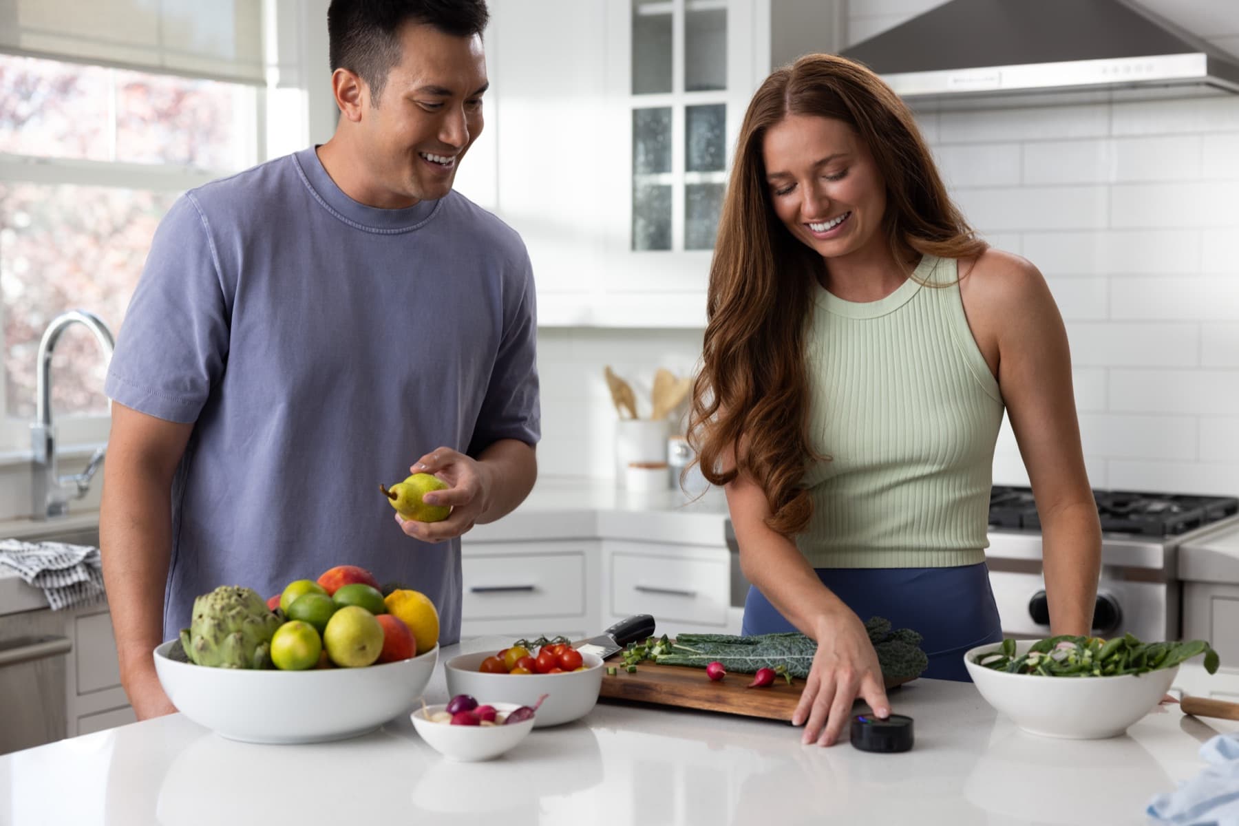 Two people sharing a joke at a kitchen counter with a bowl of produce as one rests a fingertip on the Prysm iO scanner