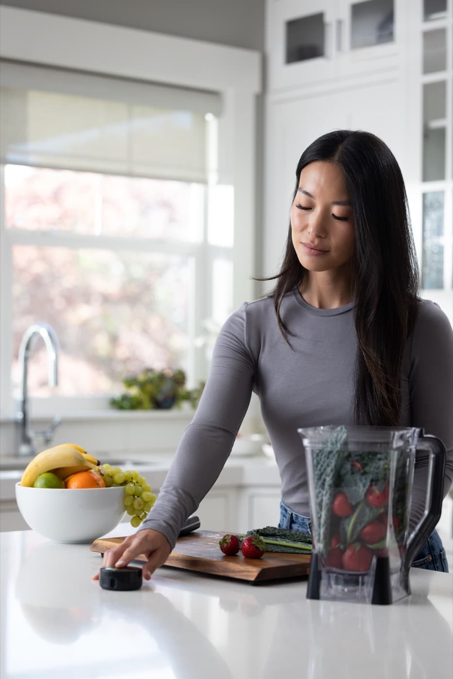 A smiling woman resting a fingertip on the Prysm iO scanner on a kitchen counter