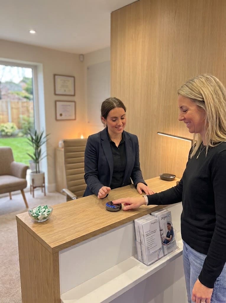 A person placing a fingertip on the Prysm iO scanner at a reception desk while a team member looks on